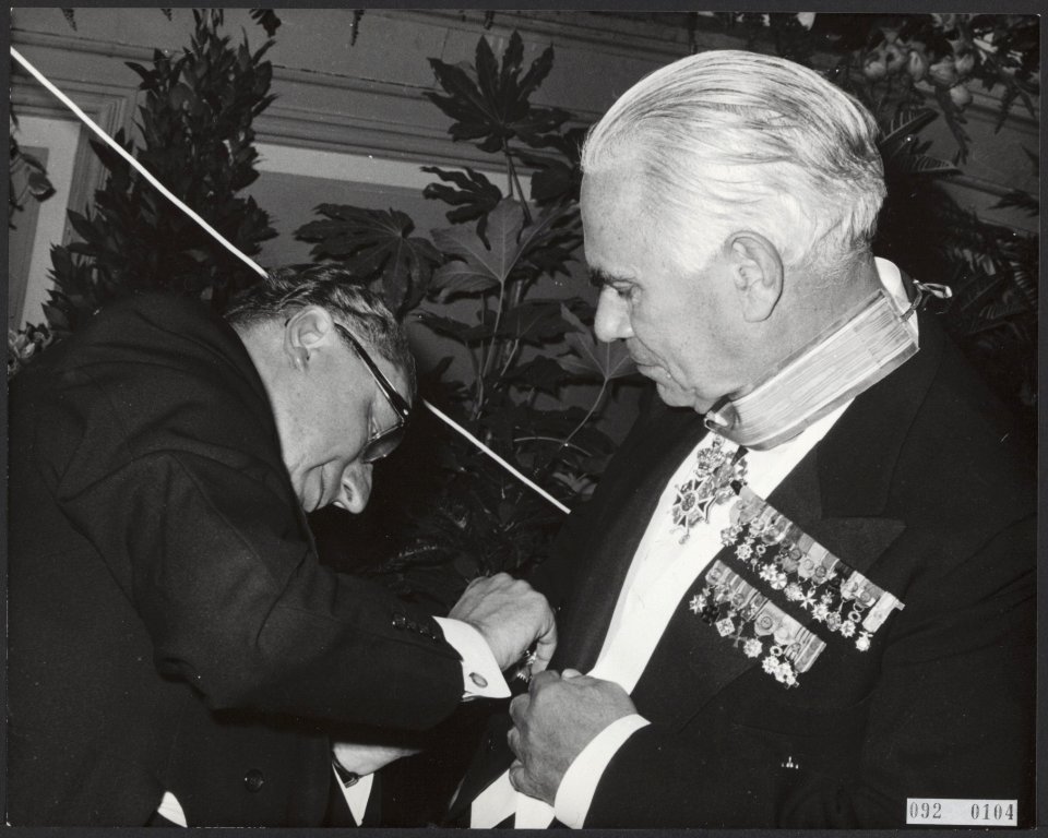 Minister J. van Aartsen (links) speldt H. Gelissen, voorzitter van de Raad van C, Bestanddeelnr 092-0104