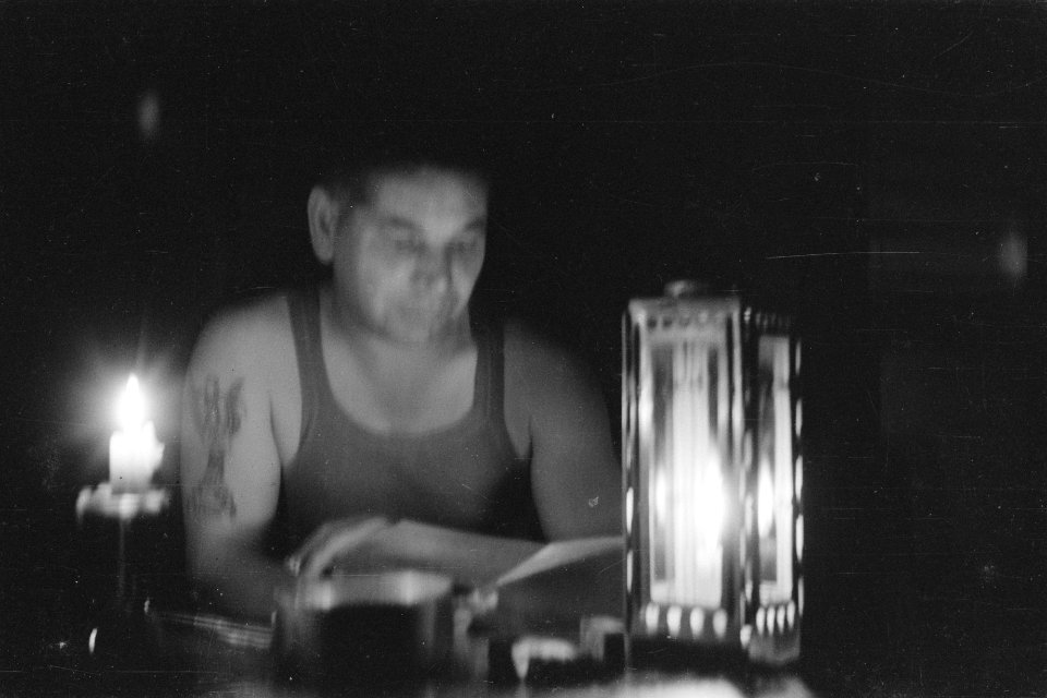 Militair in singlet en tattoo op rechterarm leest iets bij het licht van een kaa, Bestanddeelnr 335-1-3