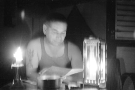 Militair in singlet en tattoo op rechterarm leest iets bij het licht van een kaa, Bestanddeelnr 335-1-4