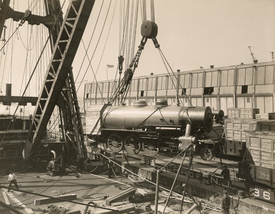 Military Administration - Transportation - Water - Miscellaneous - LOADING CONSOLIDATED LOCOMOTIVES ABOARD S.S. FELTORE, N.Y. Locomotives being hoisted off rails toward ship - NARA - 45502349 (cropped)