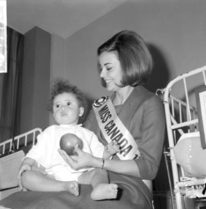 Miss Canada terwijl zij een kind op schoot heeft en het een appel aanbiedt, Bestanddeelnr 918-4774