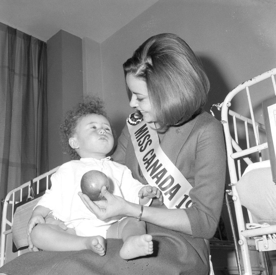 Miss Canada terwijl zij een kind op schoot heeft en het een appel aanbiedt, Bestanddeelnr 918-4770