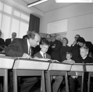Minister- president Cals terwijl hij achter een tafeltje zit, naast een leerling, Bestanddeelnr 918-3734