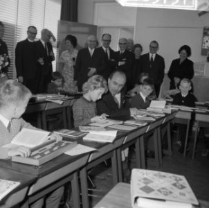 Minister-president Cals terwijl hij achter een tafeltje zit, naast een leerling…, Bestanddeelnr 918-3737