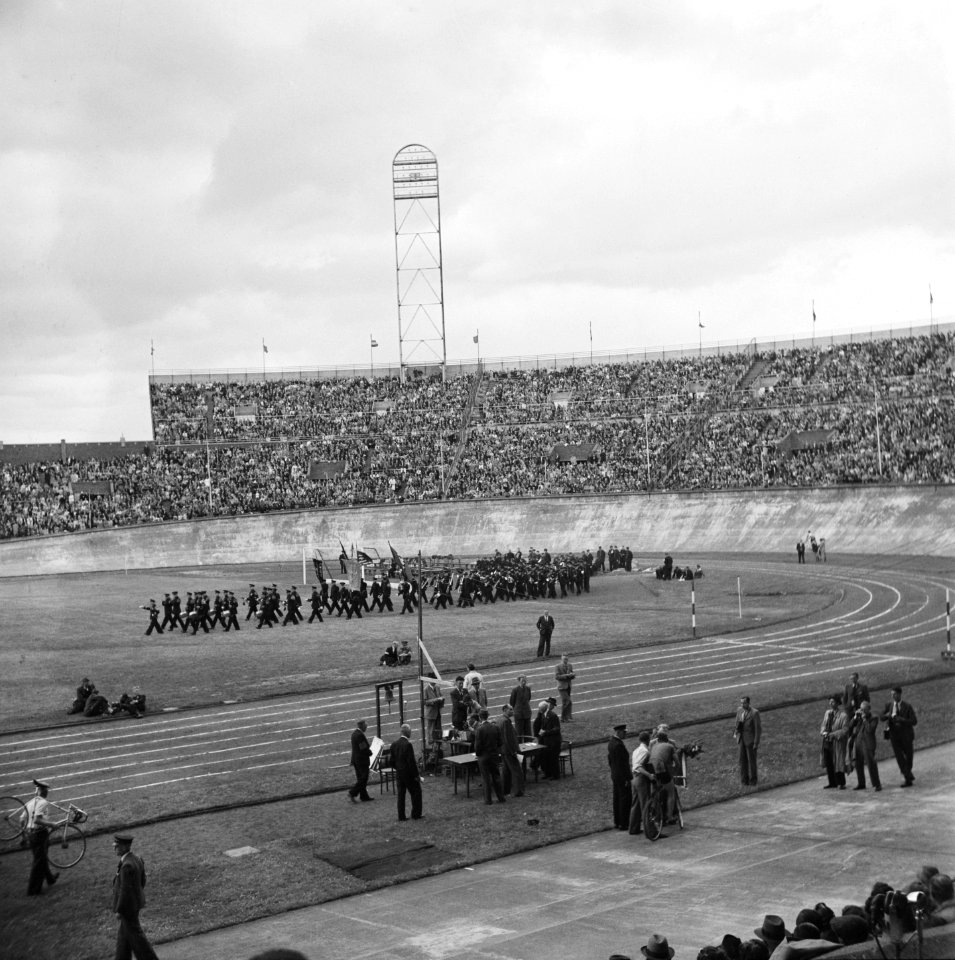 Muziekband paradeert over het veld van het Olympisch Stadion. Aan de zijkant is, Bestanddeelnr 900-4592
