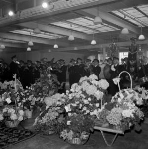 Muziekkorps tijdens uitvoering in zaal met bovenlicht, met op de voorgrond bloem, Bestanddeelnr 255-8536