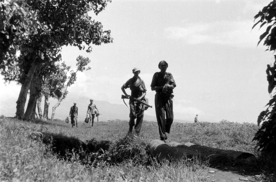 Nederlandse patrouille in open veld. Twee militairen steken een greppel over via, Bestanddeelnr 5557