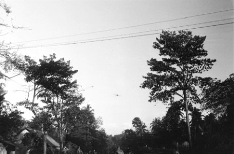 Nederlandse militairen in een kampong. In de lucht een vliegtuig, Bestanddeelnr 7277