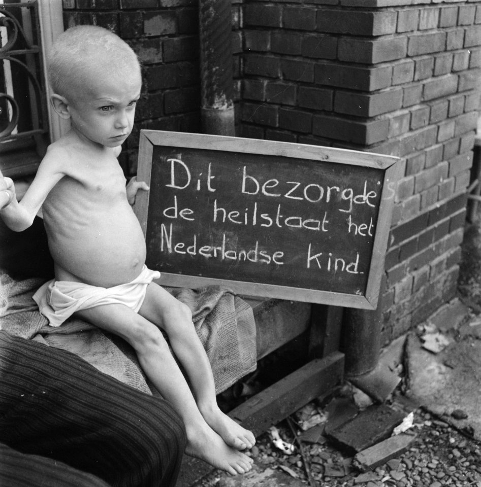 Ondervoede baby houdt een bord vast met opschrift Dit bezorgde de heilstaat het, Bestanddeelnr 900-4775
