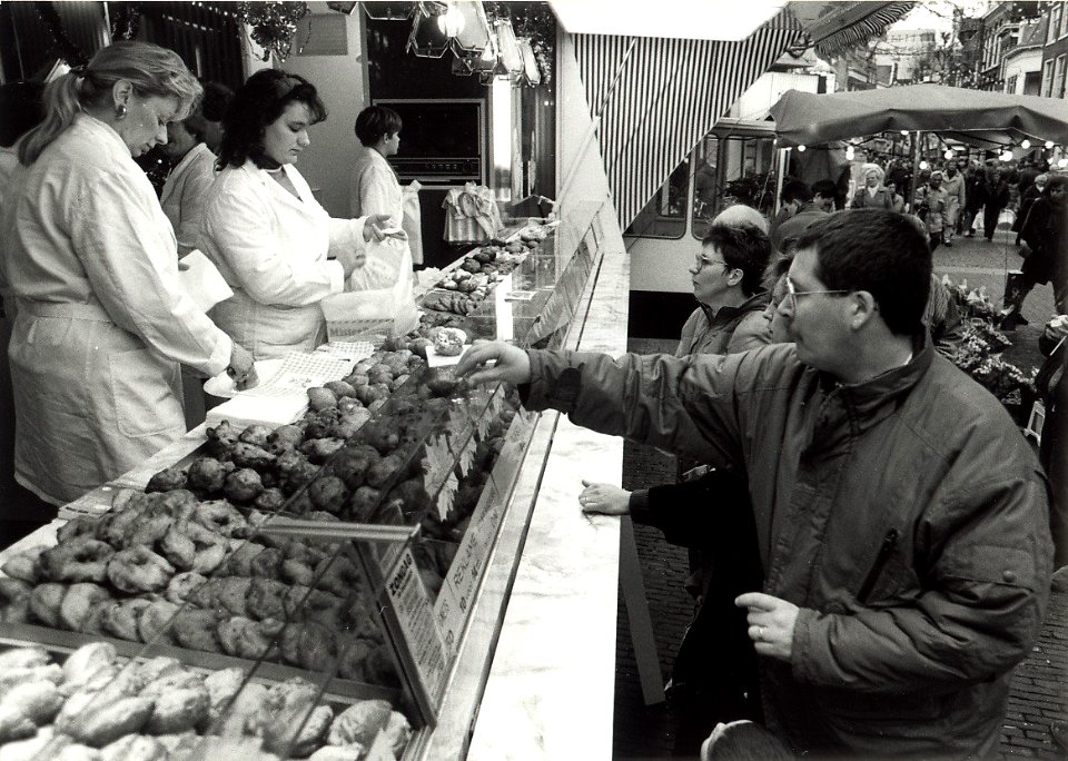 Oliebollenkraam van de Fam. Brouwer voor het Proveniershuis in de Grote Houtstraat. Aangekocht van United Photos de Boer. - Negatiefnummer 33550 k 23. - Gepubliceerd in het Haarlems Dagblad van 31.12