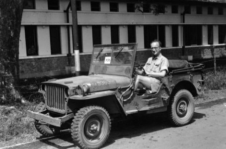Oorlogsverslagger poseert, zittend achter het stuur van een jeep (op de voorruit, Bestanddeelnr 5907
