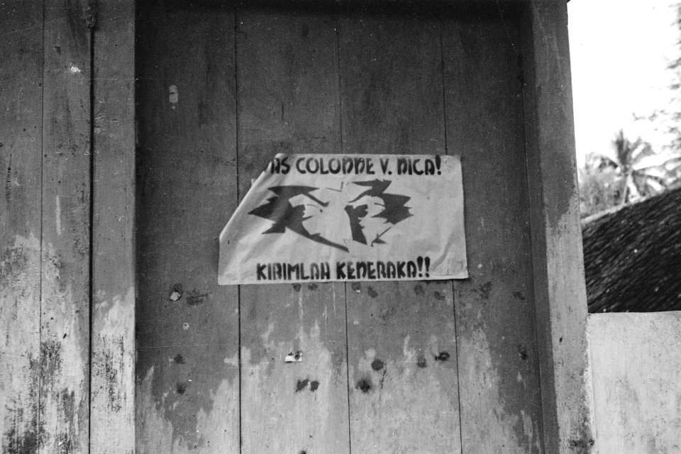 Op een barak is een poster aangeplakt met een afbeelding van twee ogen die door , Bestanddeelnr 334-5-6