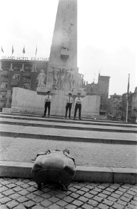 Op de voorgrond een rugzak, op de achtergrond politieagenten voor het monument, Bestanddeelnr 922-6831