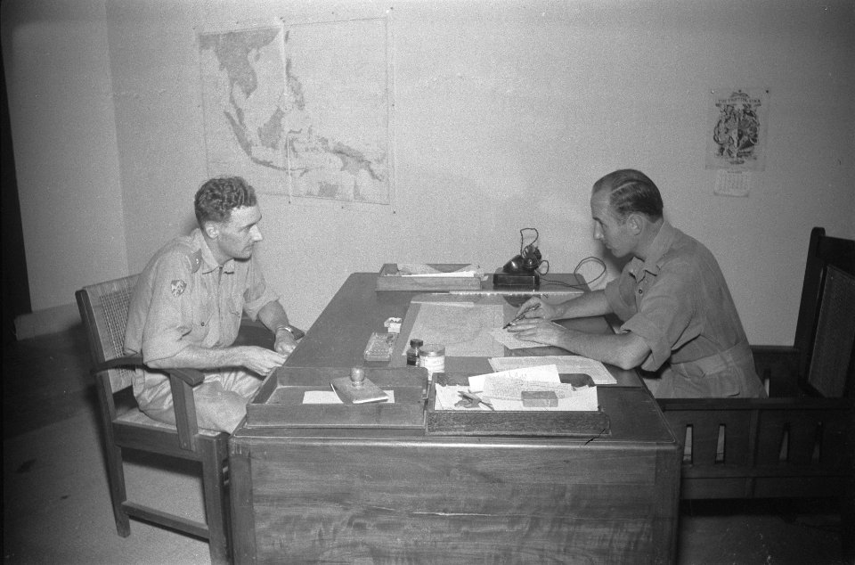 Officieren achter een bureau in een kantoor van Dienst Welfare, Bestanddeelnr 110-4-3