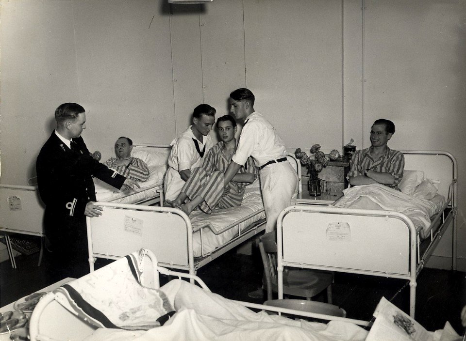 Officier van Gezondheid 3de klas, H. v.d. Velden, geeft opdracht aan twee zieken verplegers de patient naar een andere zaal over te brengen. Aangekocht in 1976 van fotograaf C. de Boer. Identificatien