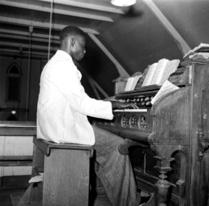 Organist in de protestantse kerk n Nieuw-Nickerie bespeelt een harmonium, Bestanddeelnr 252-5491