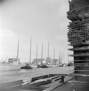 Opslag van planken met op de achtergrond huizen en schepen, Bestanddeelnr 191-0642