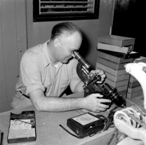 Opticien met een microscoop bij de firma Spritzer & Fuhrmann in Willemstad, Bestanddeelnr 252-3285