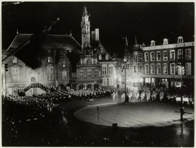 Optreden van een drumband voor het in de avond verlichte Stadhuis