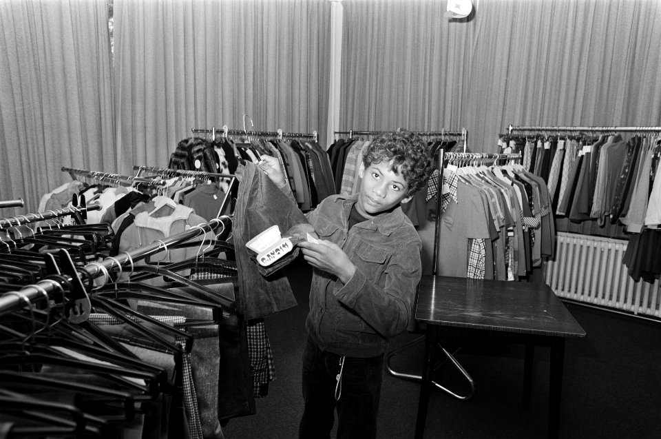 Opvangcentrum voor Surinamers in Putten jongetje tussen stapels kleding, Bestanddeelnr 927-6797