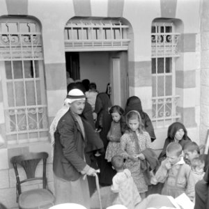 Oudere man met vrouwen en kinderen bij de ingang van een polikliniek waarvan de , Bestanddeelnr 255-0948