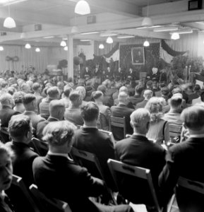 Overzicht van een zaal met zittende mensen op klapstoelen, op de achtergrond rec, Bestanddeelnr 255-8559