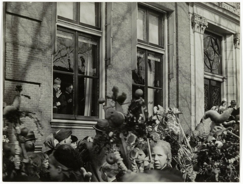 Palmpasenoptocht voor het Bisschoppelijk paleis aan de Nieuwe Gracht 80. Met mgr. J.P. Huibers wuivend achter het raam. NL-HlmNHA 54005506