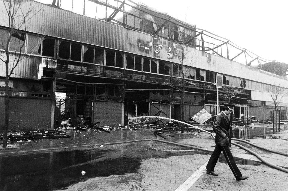 Politieagent loopt bij het door brand verwoeste winkelcentrum in Ridderkerk 27 januari 1981, Bestanddeelnr 931-2869