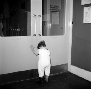 Peuter in hansop met twee verschillende schoenen aan bij een deur, Bestanddeelnr 252-9099