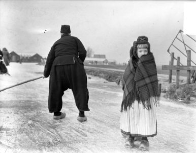 Schaatsen in Volendam. Meisje met omslagdoek. Man veegt baan op vaart schoon, Bestanddeelnr 903-8043