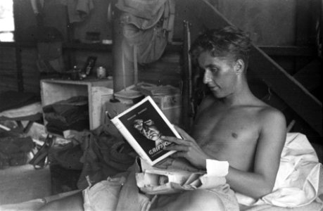Soldaat ligt in bed met een geopend pakket. In zijn handen het boek Griffioen , Bestanddeelnr 5767