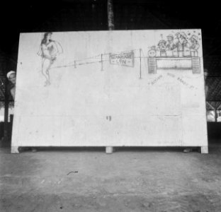 Soldaat kijkt om de hoek van een groot bord waarop een tekening voorstellende de, Bestanddeelnr 13212