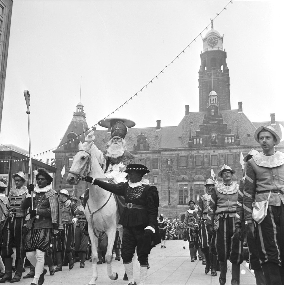 Sinterklaas terwijl hij op zijn schimmel zit voor het stadhuis, begeleid door Zw, Bestanddeelnr 918-4741