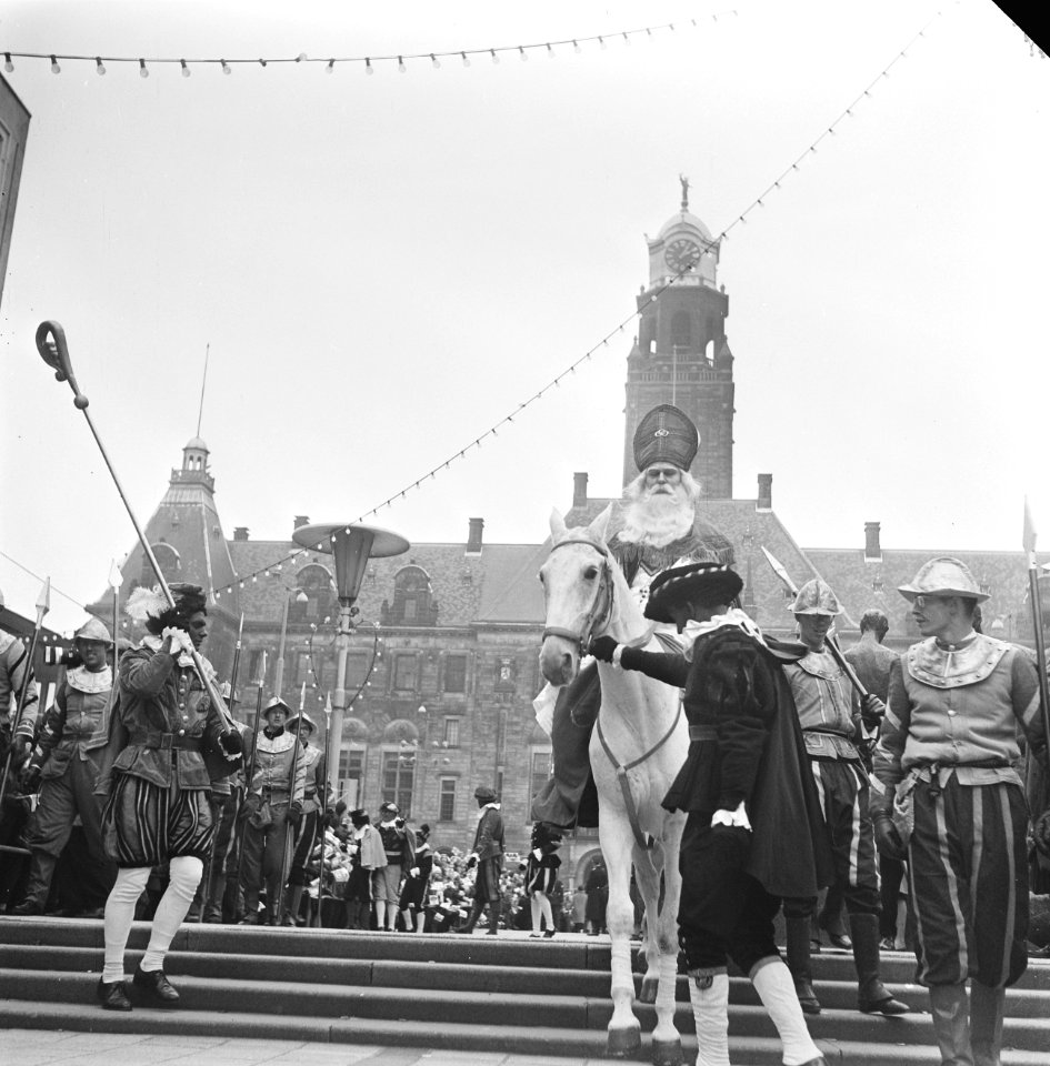 Sinterklaas terwijl hij op zijn schimmel zit voor het stadhuis, begeleid door Zw, Bestanddeelnr 918-4739