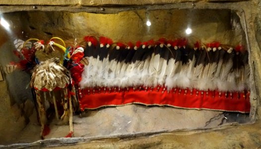 Split horn headdress, Siksika, mid 1900s, view 1, buckskin, weasel tails, glass beads, horse hair, brass bells, conch shell, porcupine quills, dew claws, red wool, eagle and down feathers - Glenbow Museum - DSC01042