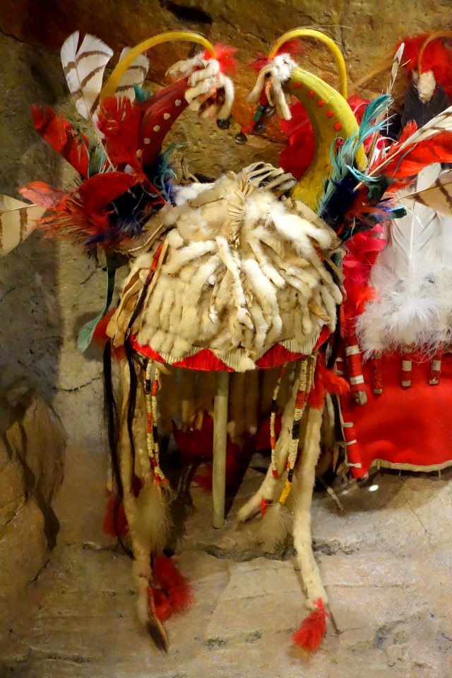 Split horn headdress, Siksika, mid 1900s, view 2, buckskin, weasel tails, glass beads, horse hair, brass bells, conch shell, porcupine quills, dew claws, red wool, eagle and down feathers - Glenbow Museum - DSC01047
