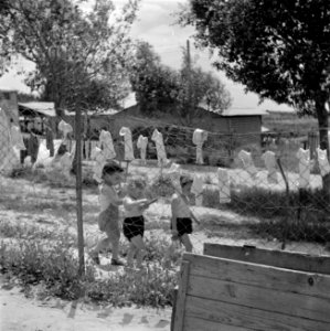 Spelende kinderen achter een hek met drogend wasgoed bij de kinderopvang van kib, Bestanddeelnr 255-0579
