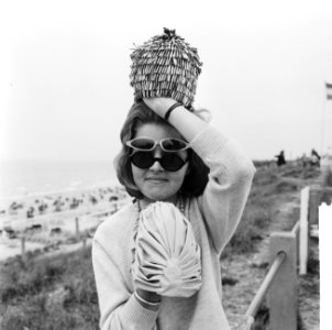 Strandmode 1964, dame toont twee zonnebrillen (fietsmodel en badmutsen, Bestanddeelnr 916-4561