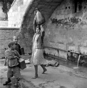 Straatbeeld in Nazareth met een Arabische vrouw met een waterkan op het hoofd en, Bestanddeelnr 255-1051