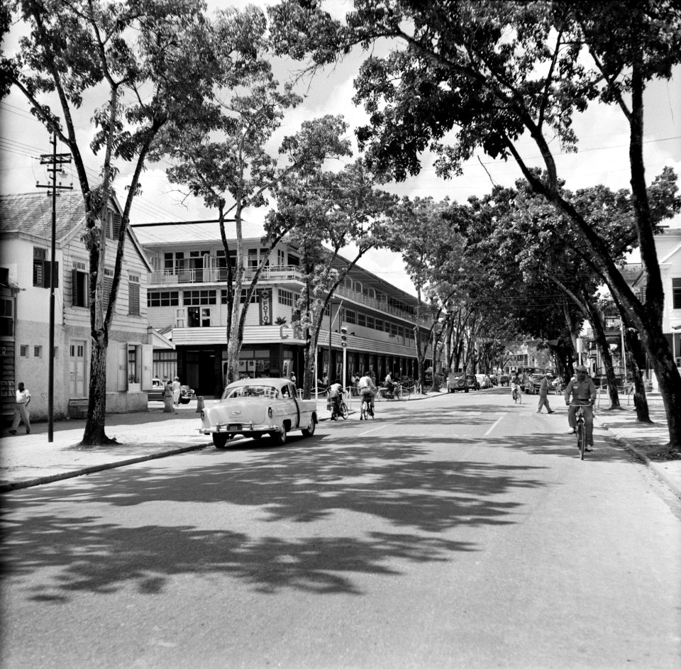Straat met winkelpand in Paramaribo met onder andere een fotowinkel en een rijwi, Bestanddeelnr 252-4945