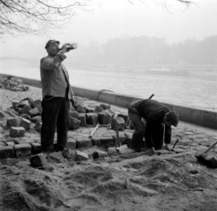 Stratenmaker drinkt uit een fles tijdens het bestraten van de kade langs de Sein, Bestanddeelnr 252-9431