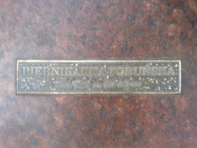 Tabliczka na cokole rzeźby Toruńska Piernikarka