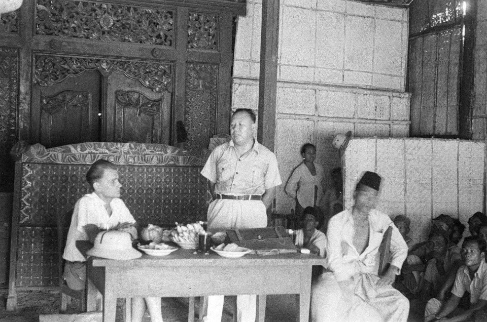 Toespraak van Indonesische man in een grote zaal met houtsnijwerk. Links een Eur, Bestanddeelnr 50-2-1