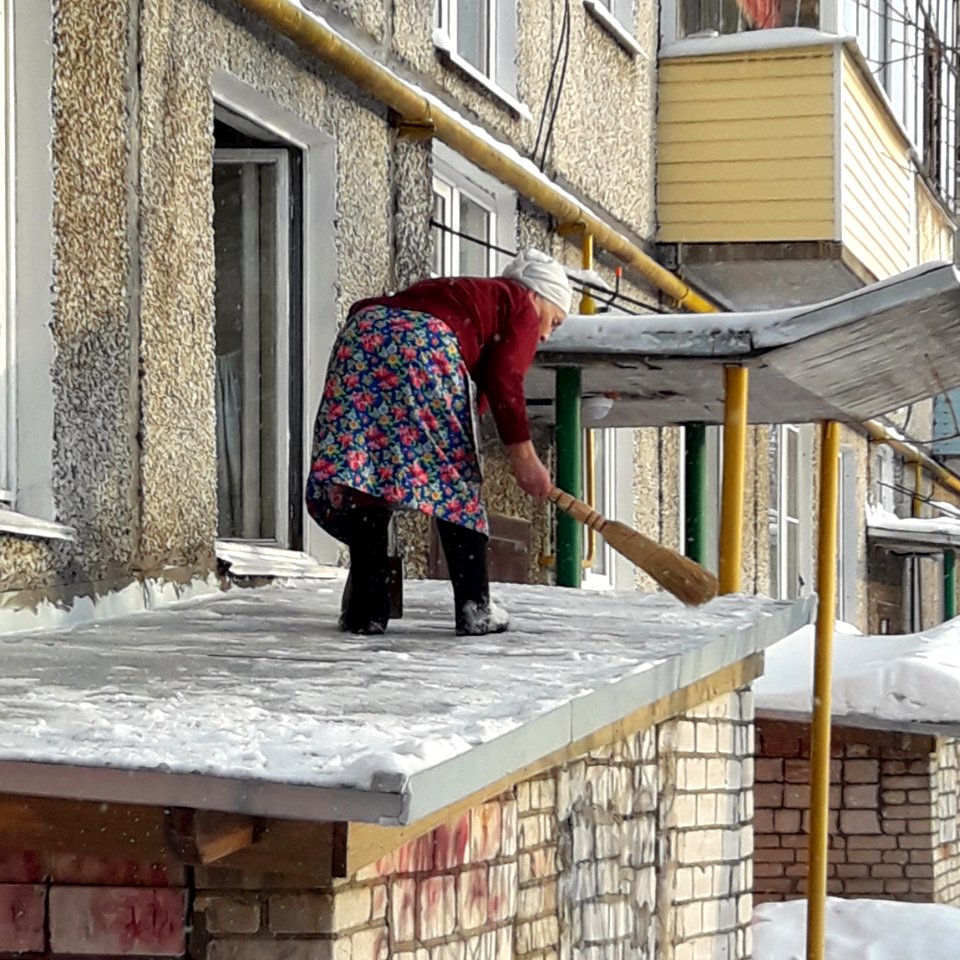 The old lady removes snow from the roof (Koryazhma)