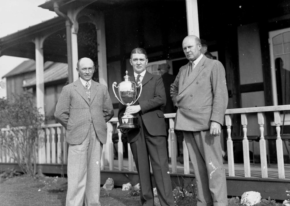 Three men outside Llandrindod Golf Club pavilion, one holding a "... Challenge Cup" (1293509)