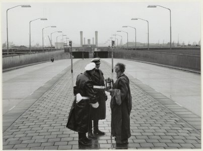 Twee agenten bij de ingang van de Velsertunnel in gesprek met een verklede man met een zandloper symbool van kortstondigheid. NL-HlmNHA 54010737