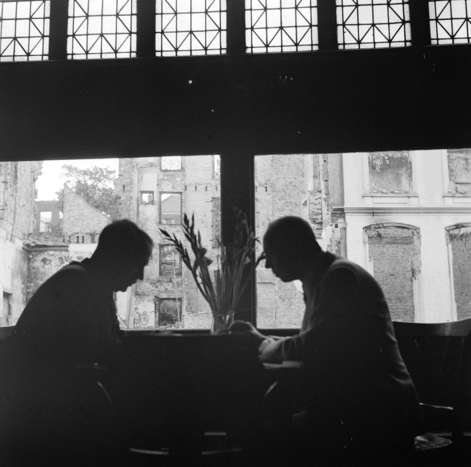 Twee mannen aan een tafel in een café-restaurant, buiten zijn de ruïnes van geb, Bestanddeelnr 900-6388