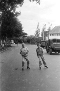Twee militairen op rolschaatsen op een brede straat. Rechts rijden twee C15TA pa, Bestanddeelnr 6309