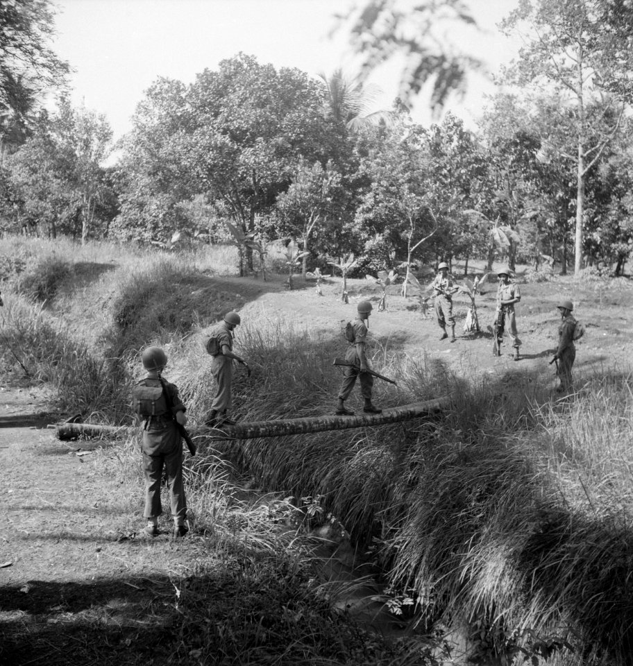 Twee militairen steken een beek of sloot over via een boomstam terwijl anderen…, Bestanddeelnr 15815