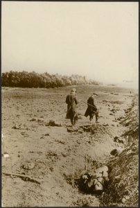 Twee militairen lopen over een veld met enige gesneuvelde soldaten, Bestanddeelnr 158-2234